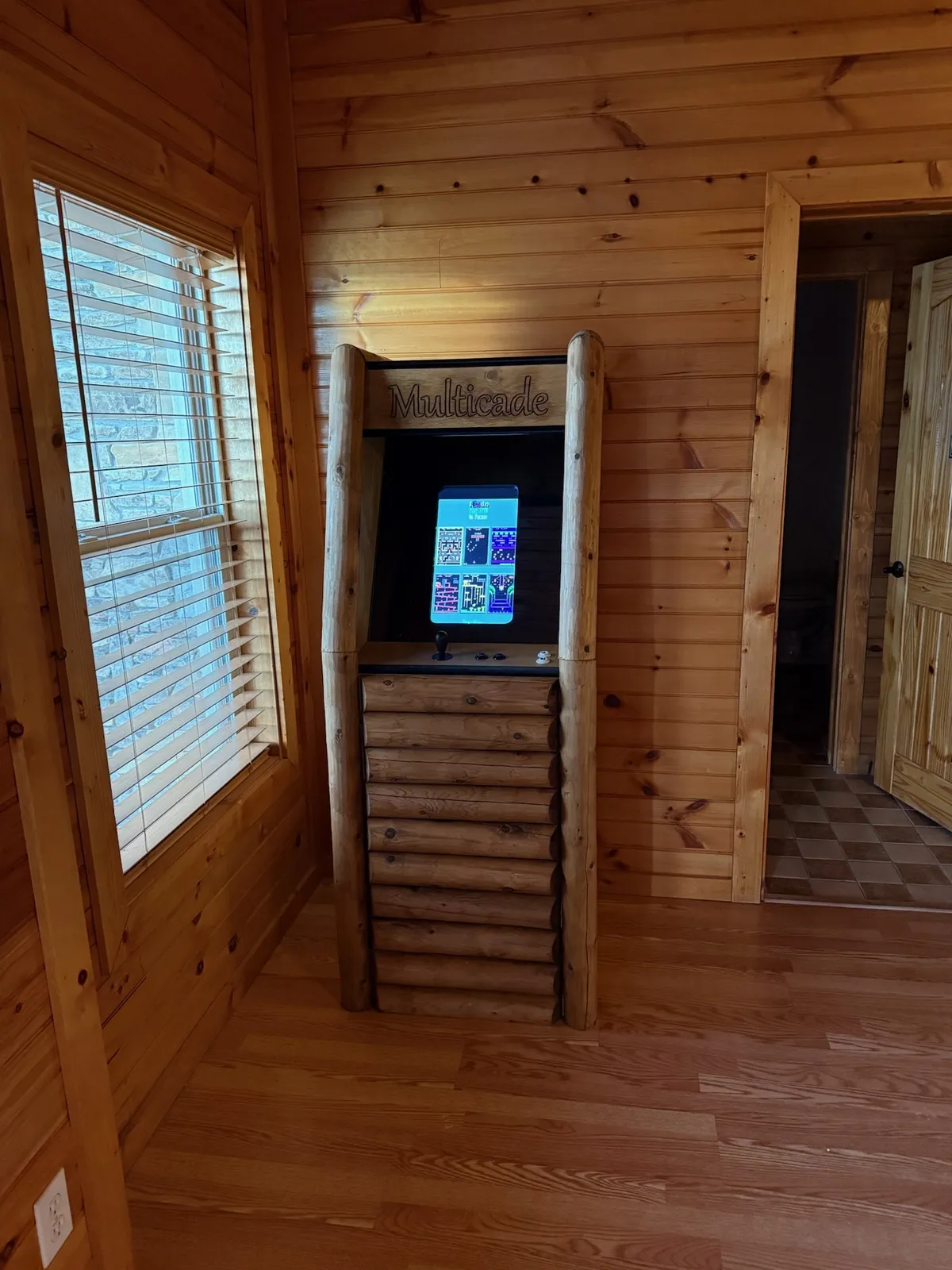 This image showcases a lively corner of the game room, featuring a Multicade arcade machine nestled against rustic wooden walls with natural light streaming in through the windows. The setup invites guests to play classic arcade games, socialize, and enjoy the nostalgic, playful atmosphere.