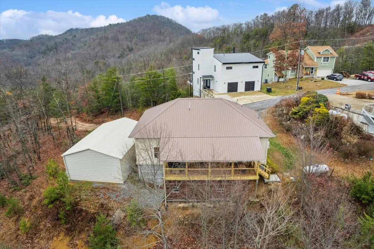 The main house is framed by lush trees with a scenic mountain view in the background. The spacious porch offers a welcoming spot for relaxation, blending the comfort of the home with the magic of nature.