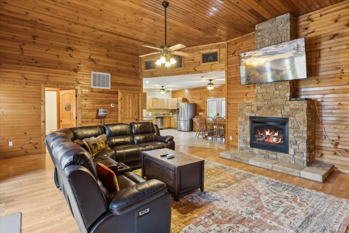 A warm, inviting interior living space with a leather sofa facing a stone fireplace, a wall-mounted TV above, and a wooden dining area nearby. The scene exudes coziness and encourages relaxation and gathering after a day spent outdoors.