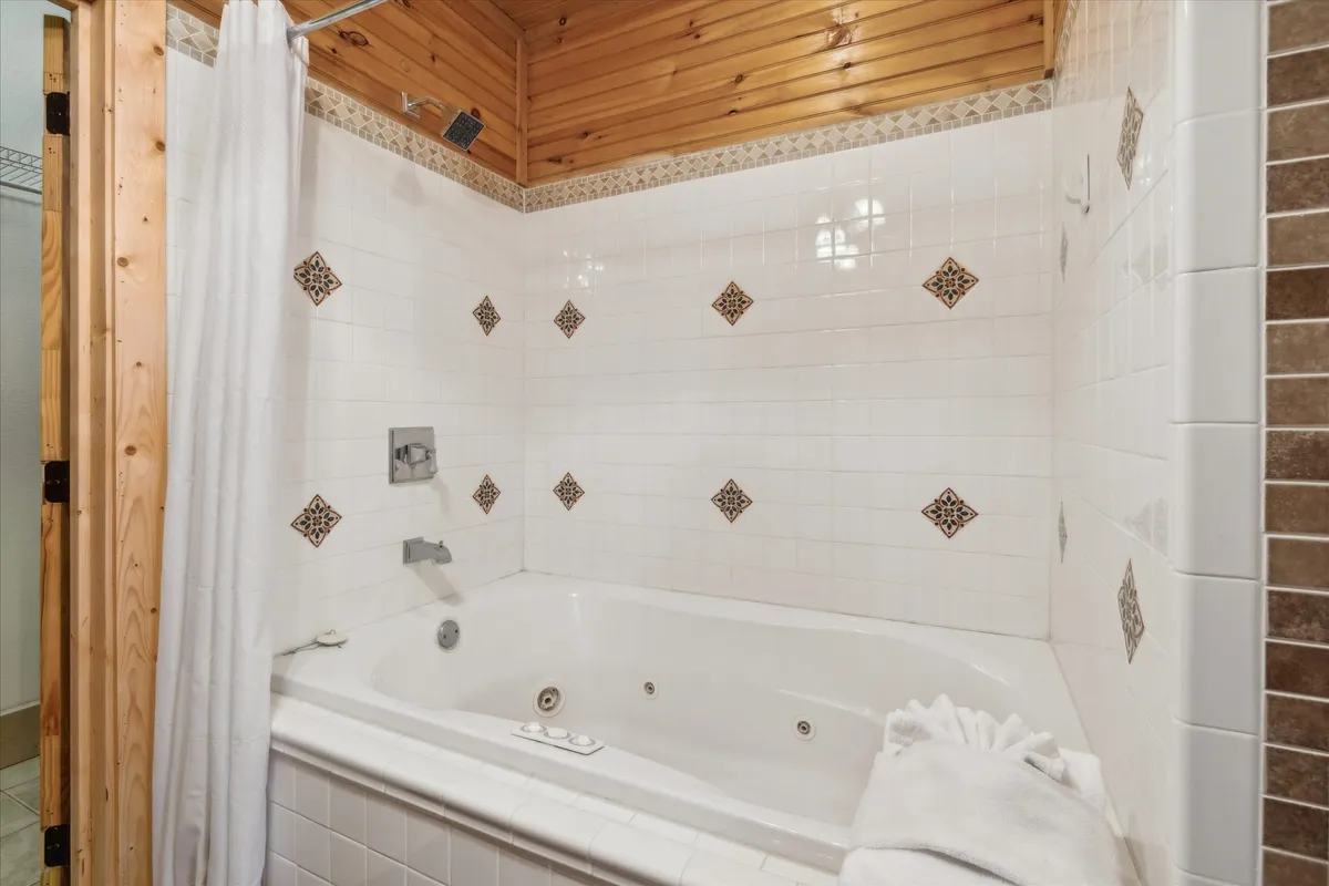 A calming bathroom space featuring a jacuzzi tub surrounded by decorative tiles, a wooden ceiling, and a shower curtain. The ambiance exudes relaxation, inviting guests to enjoy a luxurious soak after a mountain adventure.