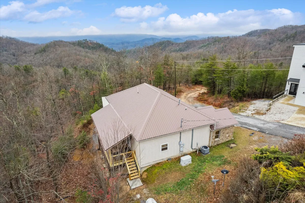 This image features the exterior of the house nestled among the Smoky Mountains and a wooded landscape. The inviting porch looks out over lush greenery, perfectly situated for morning coffee or evening relaxation while taking in sweeping mountain views.