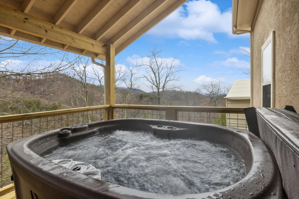 A beautiful outdoor hot tub sits under a wooden structure, perfectly positioned to take in expansive Smoky Mountain views. The scene is tranquil, with nature visible all around—ideal for relaxing soaks at sunset or under the stars.