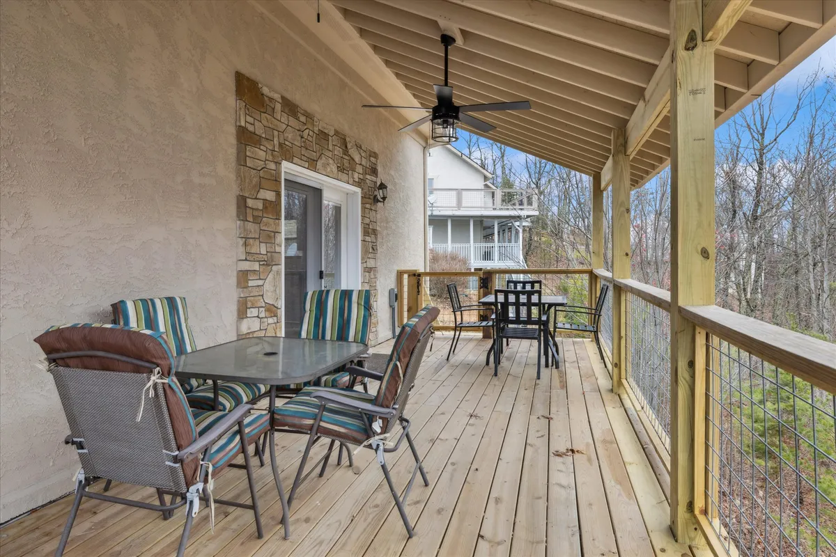 A cozy outdoor seating area on the porch features striped chairs, a glass table, and a sturdy wooden railing. The inviting setup overlooks nature, making it an ideal spot for morning coffee or gathering with friends and family.