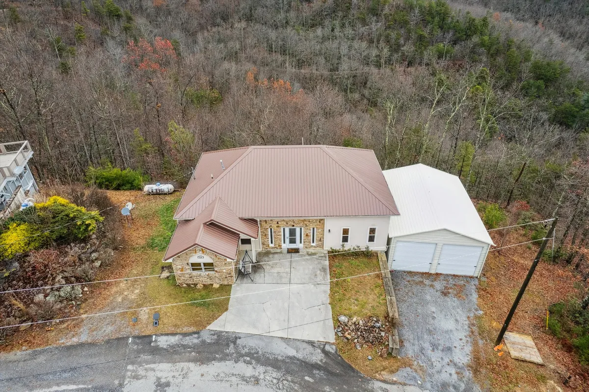 The main entrance of the house with a striking metal roof, surrounded by mature trees and featuring a detached garage. The inviting front porch hints at gatherings and easy access to the outdoors.