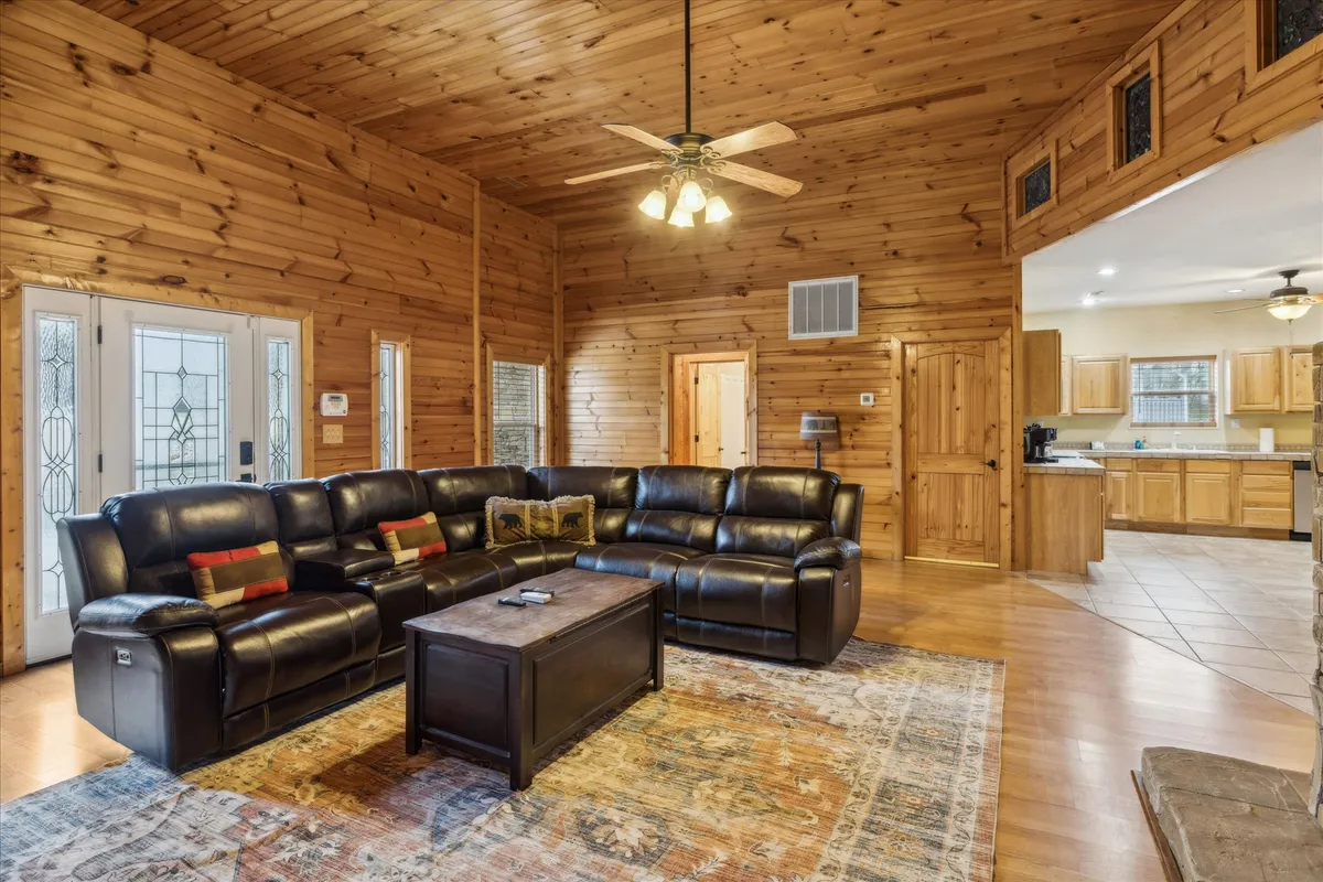 A spacious, warmly lit lounge area with a leather sectional sofa, coffee table, decorative pillows, and wooden walls. This inviting space is designed for relaxing, hosting gatherings, and playing board games or card games with family and friends.